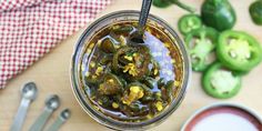 a glass jar filled with pickles next to spoons and peppers on a table