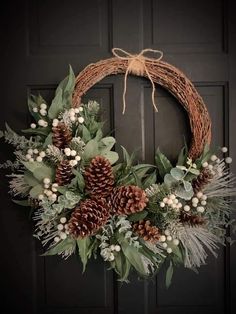 a wreath with pine cones and greenery hanging on a door