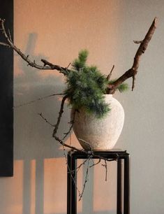 a white vase sitting on top of a metal stand next to a tree branch covered wall