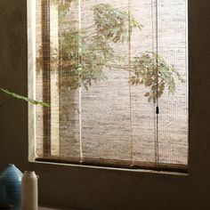 a window with bamboo blinds in front of it and a vase on the other side