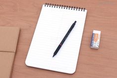 a notepad and pen sitting on top of a wooden table next to an eraser