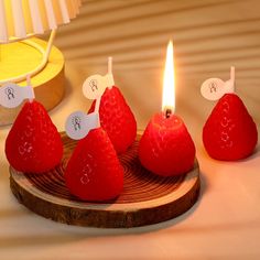 four strawberries are sitting on a wooden plate with one lit candle in the middle