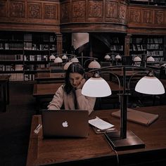 a woman sitting in front of a laptop computer on top of a desk next to a lamp