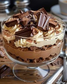 a dessert dish with chocolate and whipped cream toppings on a wooden table next to utensils