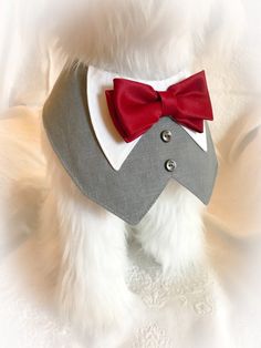 a white teddy bear wearing a red bow tie and gray shirt with silver buttons on it