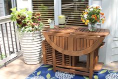 a wooden table sitting on top of a porch next to a vase filled with flowers