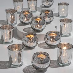 many glass candles are lit on a white table