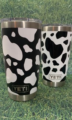 two yeti travel mugs sitting on top of a green grass covered field next to each other