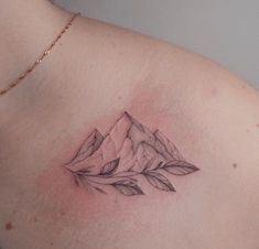 a woman's chest with a mountain and leaves tattoo on her left side shoulder