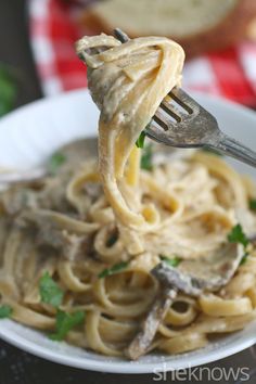 a fork full of pasta with mushrooms and parsley on top, being lifted from a white plate