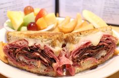 a sandwich with meat, cheese and fruit on a plate next to some french fries