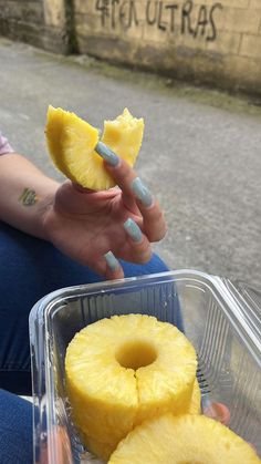 a person sitting on the ground with some food in their hand and one piece of pineapple