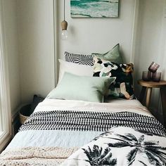 a bed with pillows and blankets on top of it next to a painting hanging above the bed