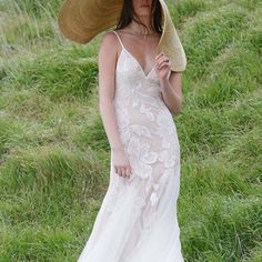 a woman in a white dress and straw hat walks through the grass with her hand on her hip