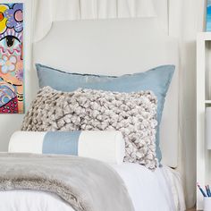 a white bed topped with pillows next to a book shelf