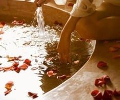 a person is washing their hands in a bathtub filled with rose petals