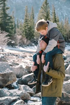 a man carrying a young boy on his shoulders while walking through some rocks in the snow