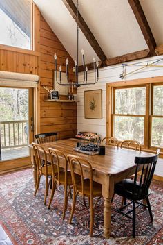 a dining room table and chairs in front of a window with wood paneling on the walls