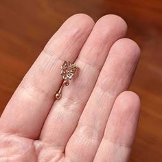 a person's left hand holding a tiny gold butterfly earring on top of a wooden table