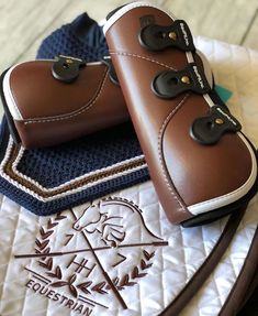 two pairs of brown leather shoes sitting on top of a white and blue blanket next to each other