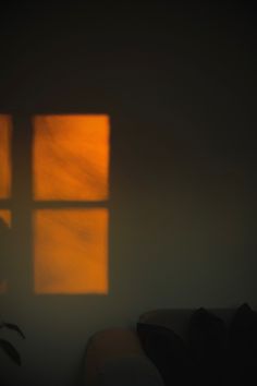 an orange light shining through a window in a dark room with a couch and chair