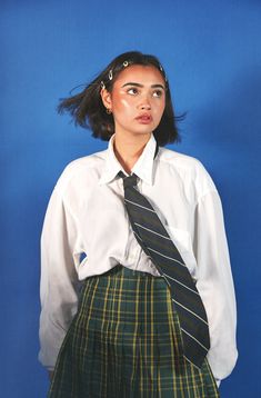 a young woman wearing a skirt and shirt with a tie on her head is posing for the camera