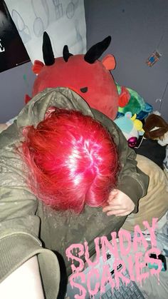 a person with red hair laying on a bed next to a stuffed animal and other toys