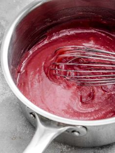 a metal pot filled with red liquid and whisk