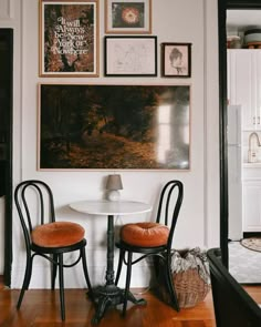 two chairs and a table in a room with pictures on the wall above them,