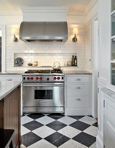 a white kitchen with black and white checkered flooring, stainless steel range hood over the stove