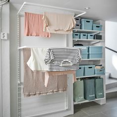 clothes hanging on racks in a closet with blue bins and white shelving units