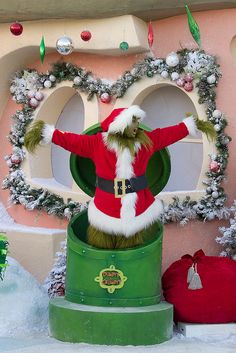 there is a santa clause standing on top of a green barrel in front of a building