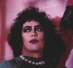 a woman with black makeup and pearls on her head is standing in front of a tiled wall