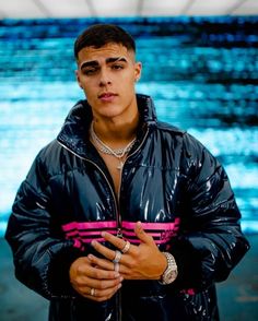 a man in a black and pink jacket with his hands on his chest looking at the camera