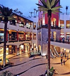 the interior of a shopping mall with palm trees in front of it and people walking around