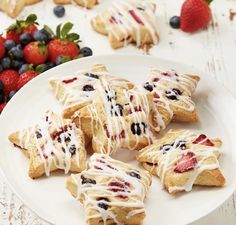 a white plate topped with pastries covered in icing next to berries and strawberries