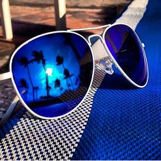 a pair of sunglasses sitting on top of a blue table next to a chair with palm trees reflected in it