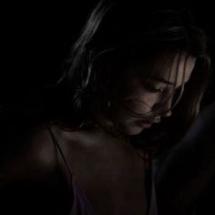 a woman in the dark with her eyes closed looking down at something on her phone