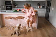 a woman sitting at a kitchen counter next to a dog and eating watermelon