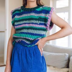 a woman standing in front of a white couch wearing blue pants and a colorful sweater