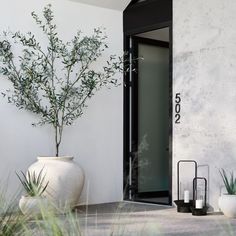 a white vase sitting on top of a cement floor next to a plant and door