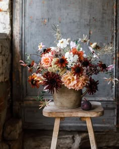 a vase filled with lots of flowers sitting on top of a wooden stool