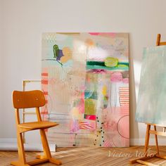 an easel sitting next to a painting on the wall and another chair in front of it