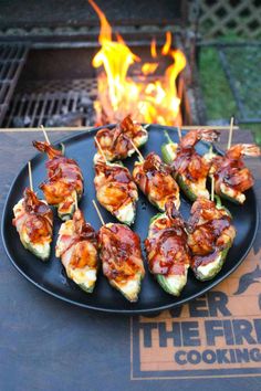 several skewered food items on a black plate with flames in the back ground