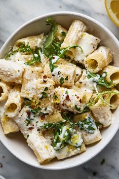 a white bowl filled with pasta covered in cheese and herbs next to lemon wedges