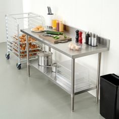 a stainless steel table with food on it in a white tiled room next to a black trash can