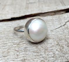 This elegant and stately pearl ring is made from a beautiful and unique white cream 14mm Mabe South Sea AAA Pearl that has many hues including pink. The pearl has been set in sterling silver with a sterling silver ring band handmade from half dome wire. This ring has some height, the setting is almost 1/2 inch high. The white cream pearl is more matte than the other mabe pearls listed, but still has a luminescent quality that makes it captivating! Made to order! Choose your size and your color p White Oval Pearl Ring, White Pearl Drop Ring, White Oval Cabochon Pearl Ring, White Oval Pearl Ring With Cabochon, Handmade White Oval Pearl Ring, White Oval Pearl Ring Gift, White Oval Pearl Ring As A Gift, White Oval Pearl Drop Rings, White Pearl Ring Gift