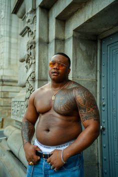 a man with tattoos on his chest standing in front of a building