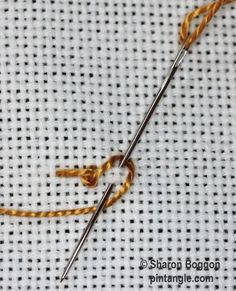 a close up of a needle and thread on a piece of white fabric with yellow stitching