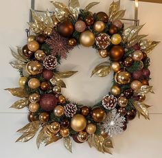 a wreath with gold and red ornaments hanging on the wall next to a candle holder